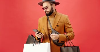 man in a brown blazer carrying shopping bags while using his cell phone