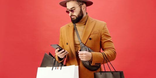 man in a brown blazer carrying shopping bags while using his cell phone