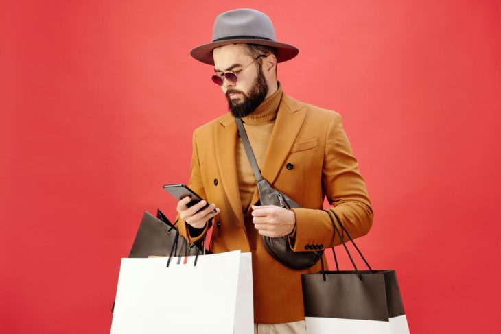 man in a brown blazer carrying shopping bags while using his cell phone