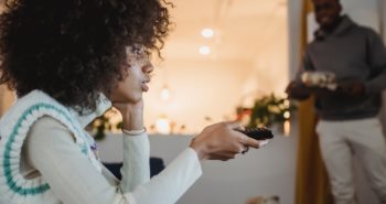 young black woman watching tv with interest near boyfriend standing in room