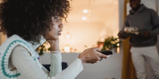 young black woman watching tv with interest near boyfriend standing in room